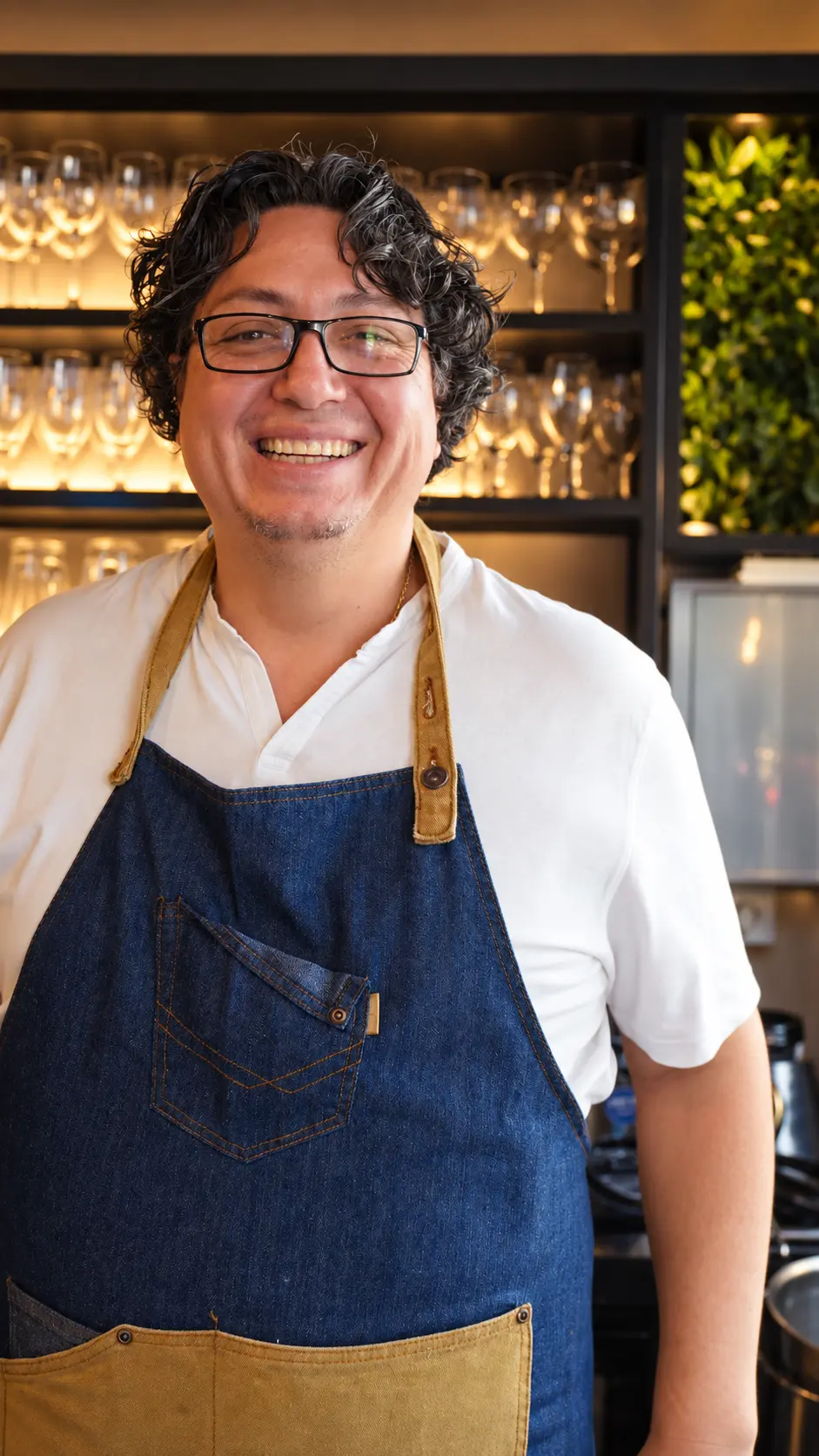 Chef de Latitud Cero sonriendo con delantal frente a la cristalería
