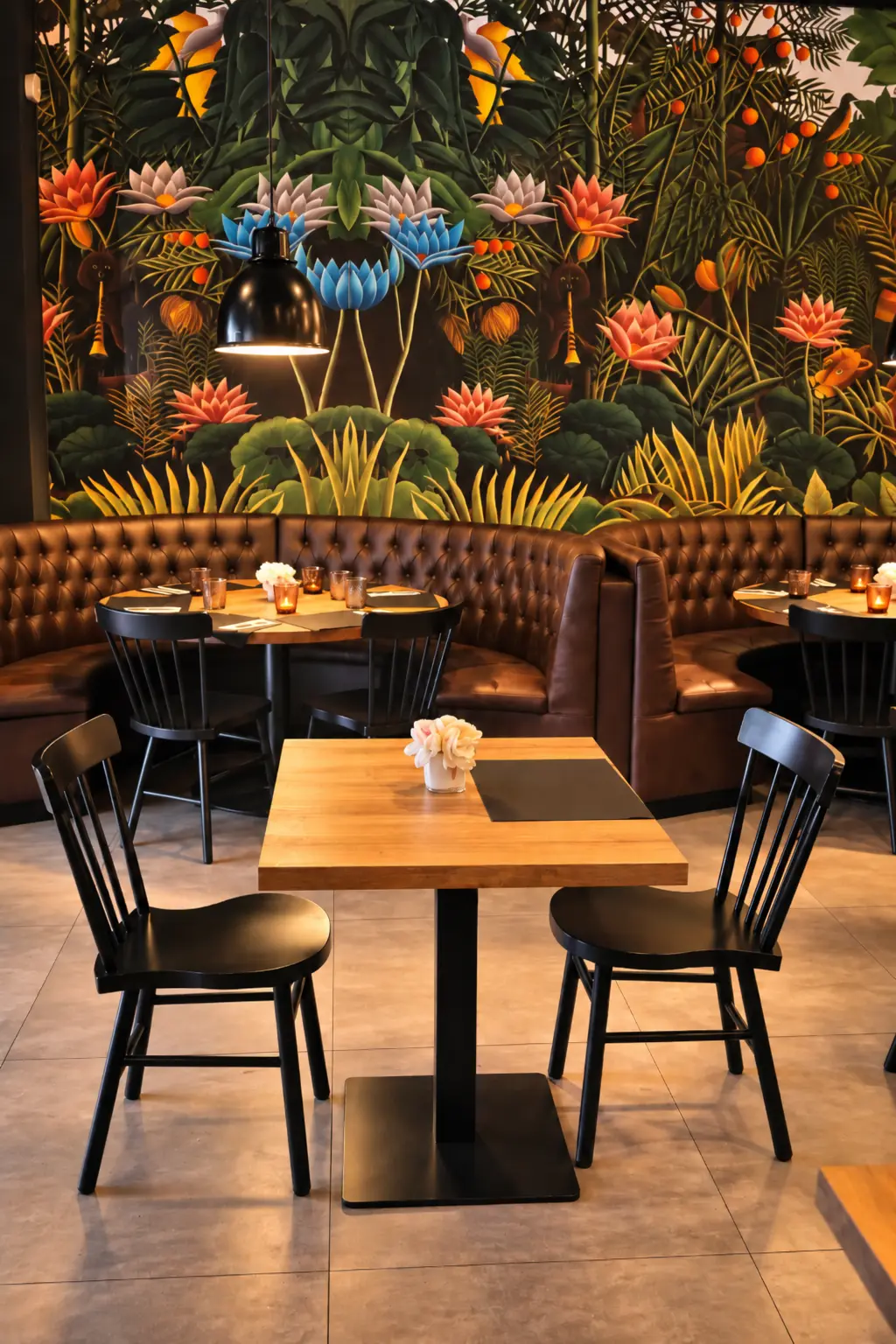 Mesa de madera y sillas negras ante el mural tropical en Rubí