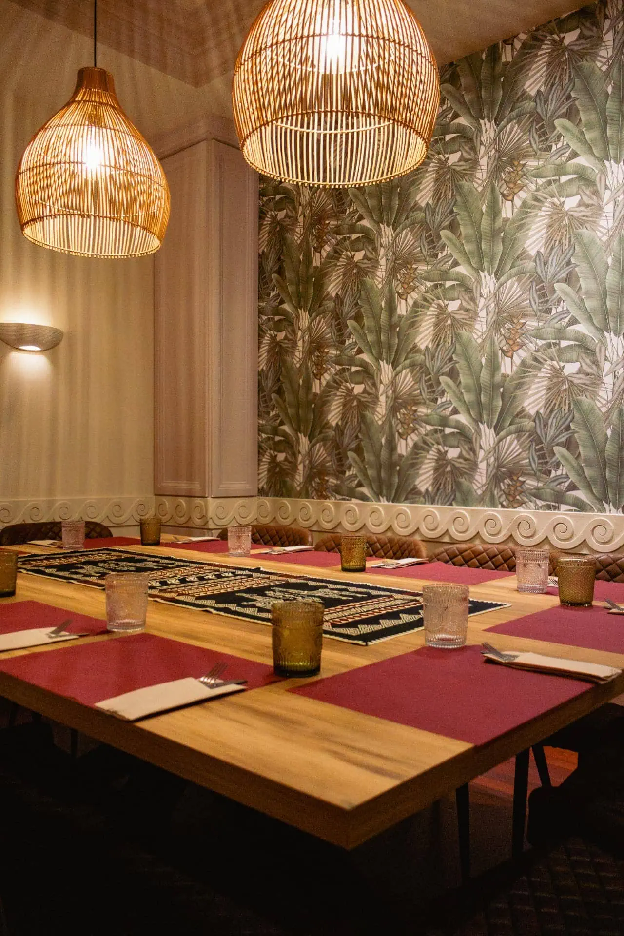 Mesa larga con lámparas de mimbre y mural tropical en Sabadell